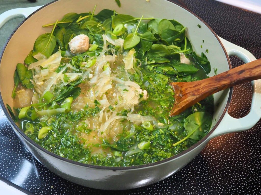 Stirring fresh greens into a dutch oven of gut-healing, anti-inflammatory ginger turkey noodle soup