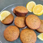 Gluten-free lemon poppy seed muffins on a cake platter with fresh lemon slices