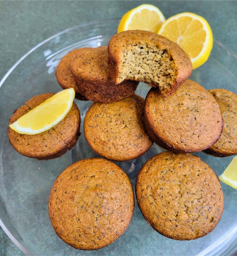 Gluten-free, dairy-free, refined sugar-free Lemon Poppy Seed Muffins on a cake platter with fresh lemon slices.