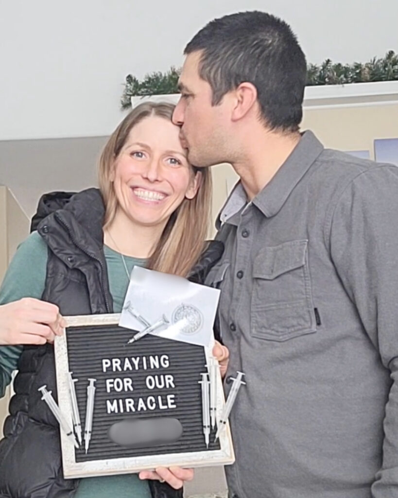Photo of the author and husband holding a sign that says "praying for our miracle" while going through infertility treatments
