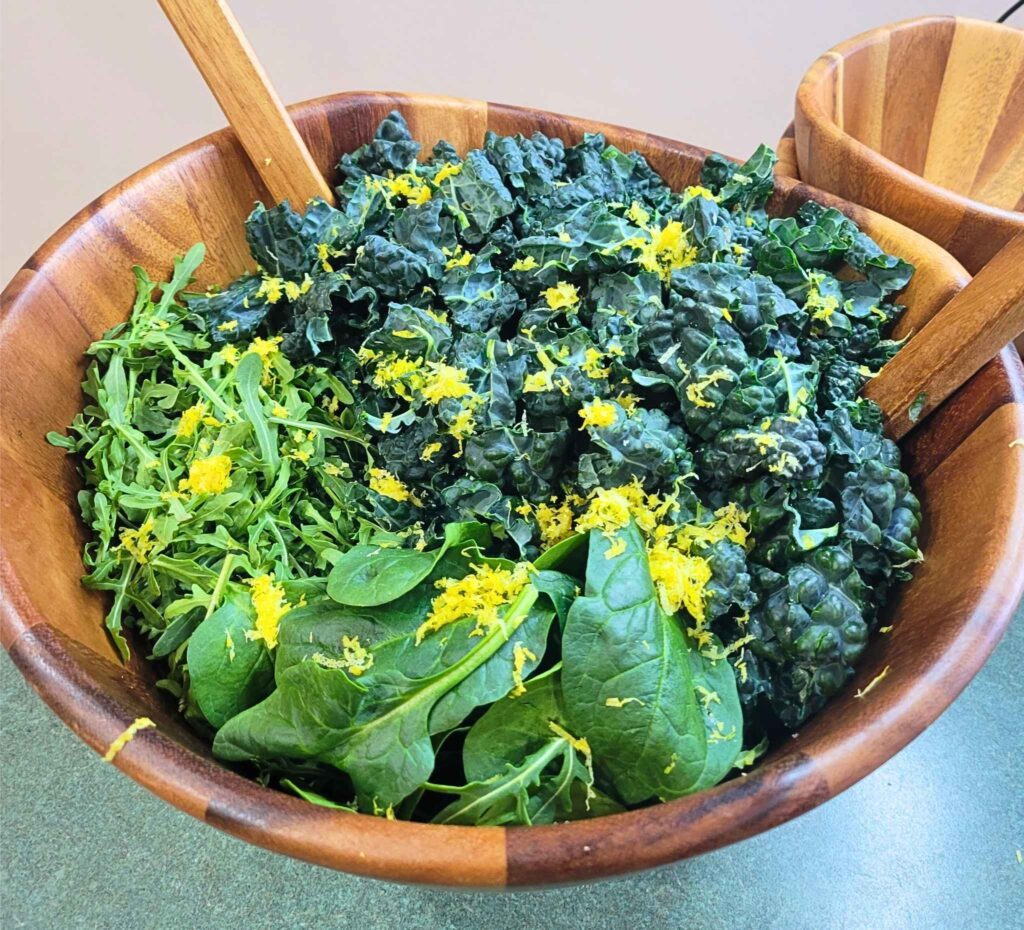 In process, making the zesty super greens salad, a bowl of lacinato kale, spinach, arugula, and lemon zest.