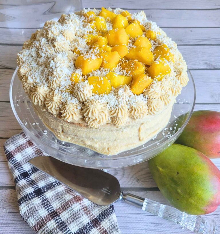 Gluten-free Mango Vanilla Cake with Dairy-free Coconut Cream frosting on a cake platter with fresh mangoes