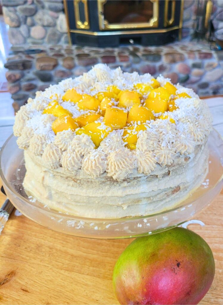 Cake platter display of gluten-free mango vanilla cake with dairy-free coconut cream frosting, topped with fresh mango chunks and shredded coconut