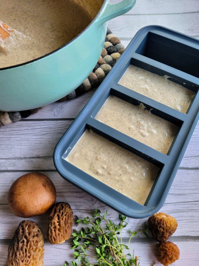 dairy-free cream of mushroom soup in soup cube trays, next to fresh morel mushrooms, cremini, and thyme.