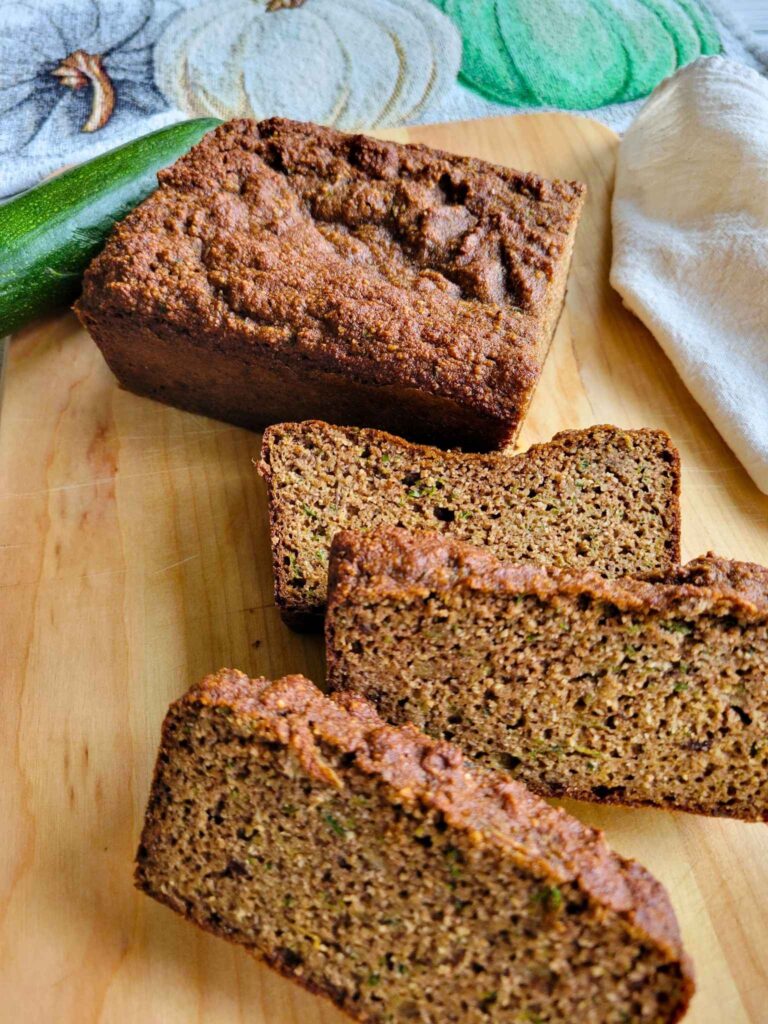 A loaf of gluten-free zucchini bread with a few slices of the bread and fresh zucchini