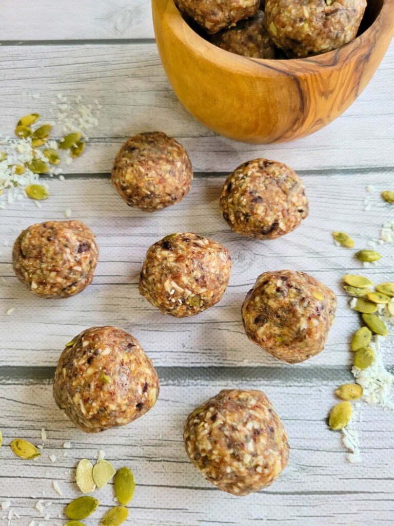 Several gut-healthy almond butter energy bites laying out with sprouted pumpkin seeds and shredded coconut